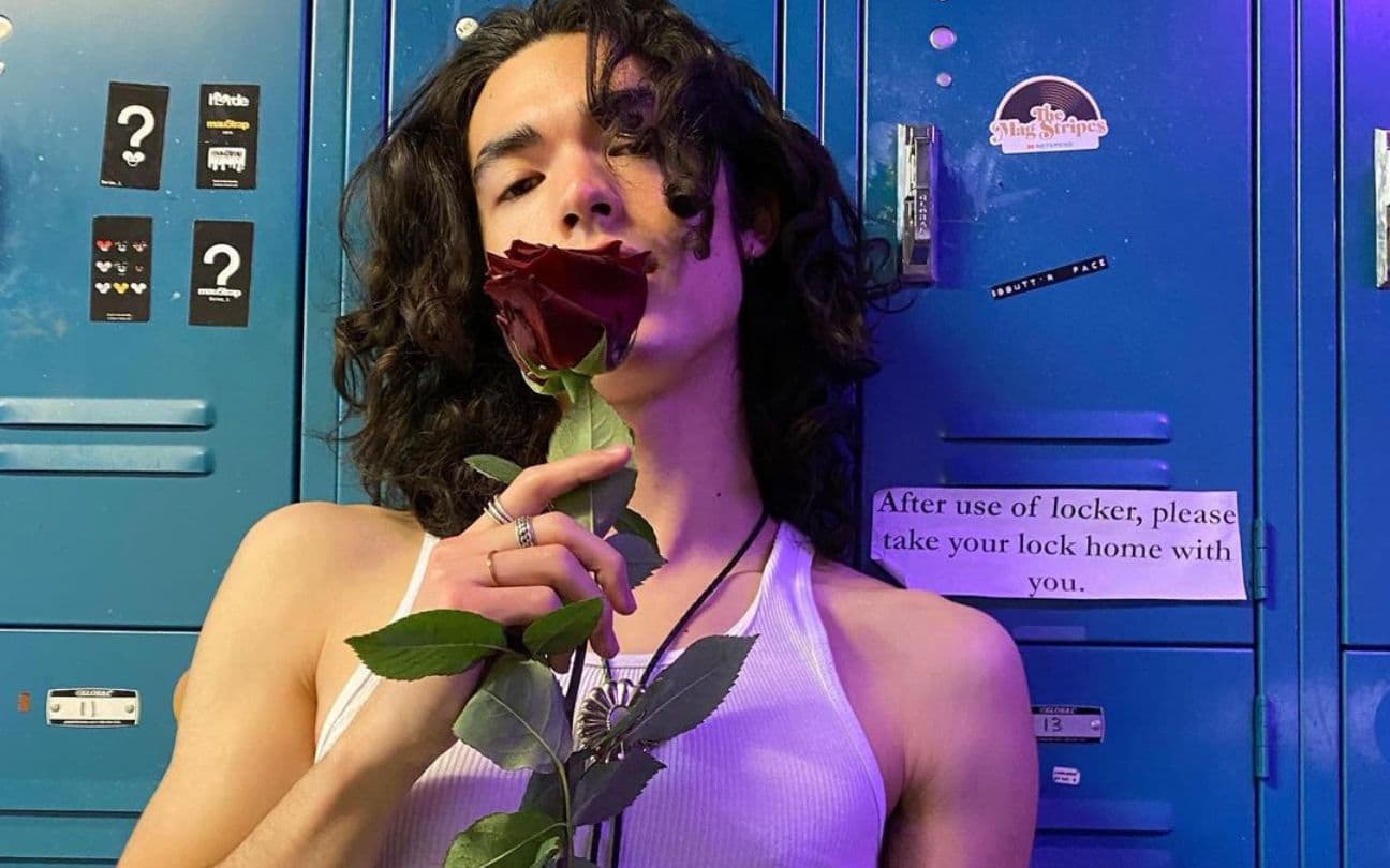 Conan Gray encostado em um armário, segurando uma rosa vermelha