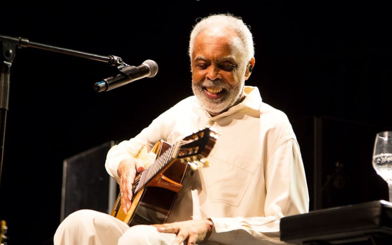 Gilberto Gil sorri, enquanto segura violão em show