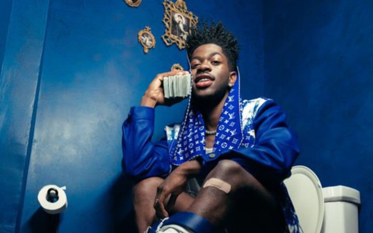Lil Nas X segura um telefone na orelha, sentado em um vaso sanitário