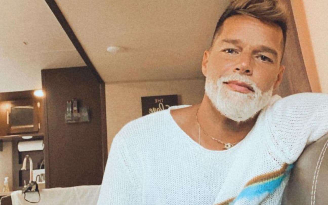 Ricky Martin sorri para foto sentado em um sofá