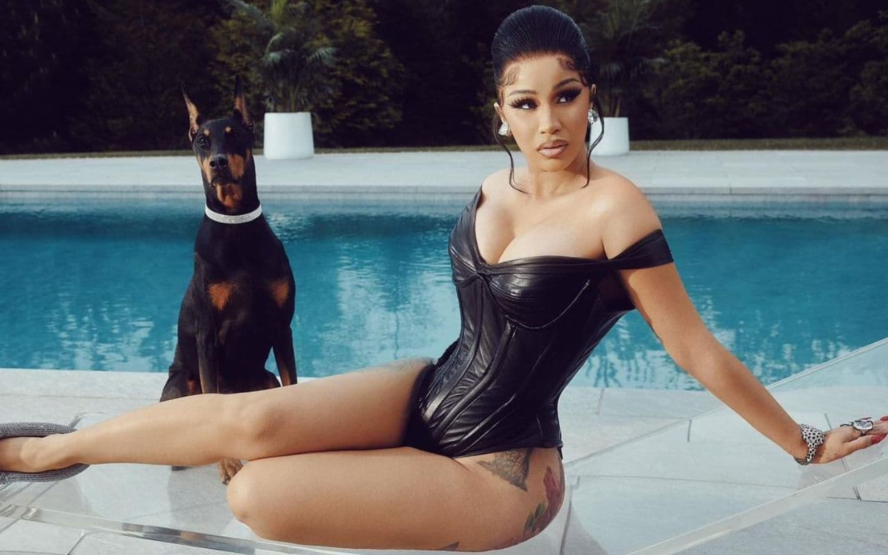 Cardi B sentada em uma espreguiçadeira, ao lado de um cachorro