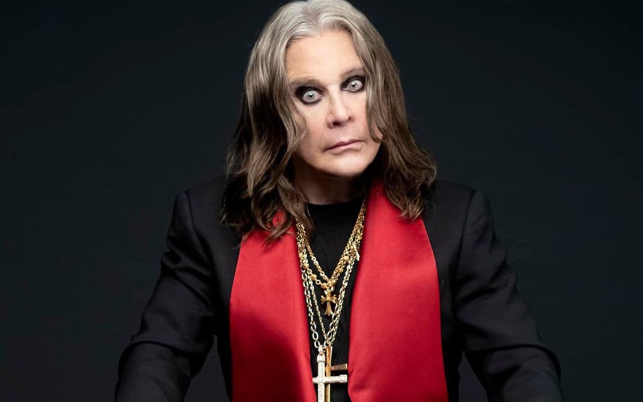 Ozzy Osbourne posa em estúdio, sentado, usando colares com crucifixos