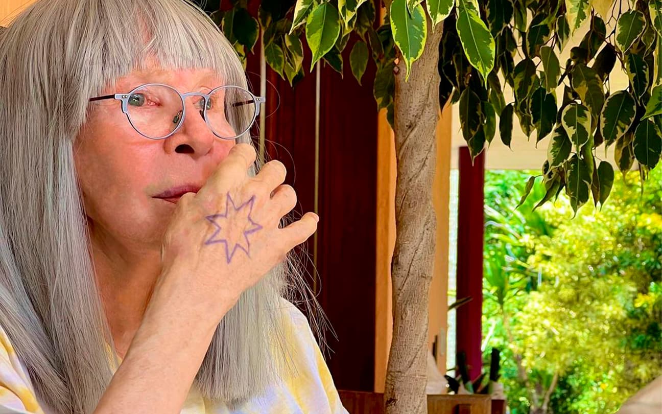Rita Lee sentada, mostrando tatuagem de estrela na mão