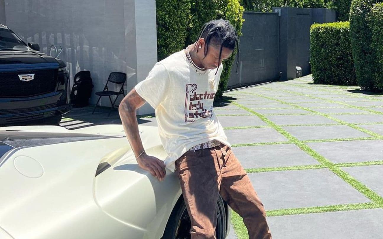 Travis Scott encostado em um carro no quintal de uma casa