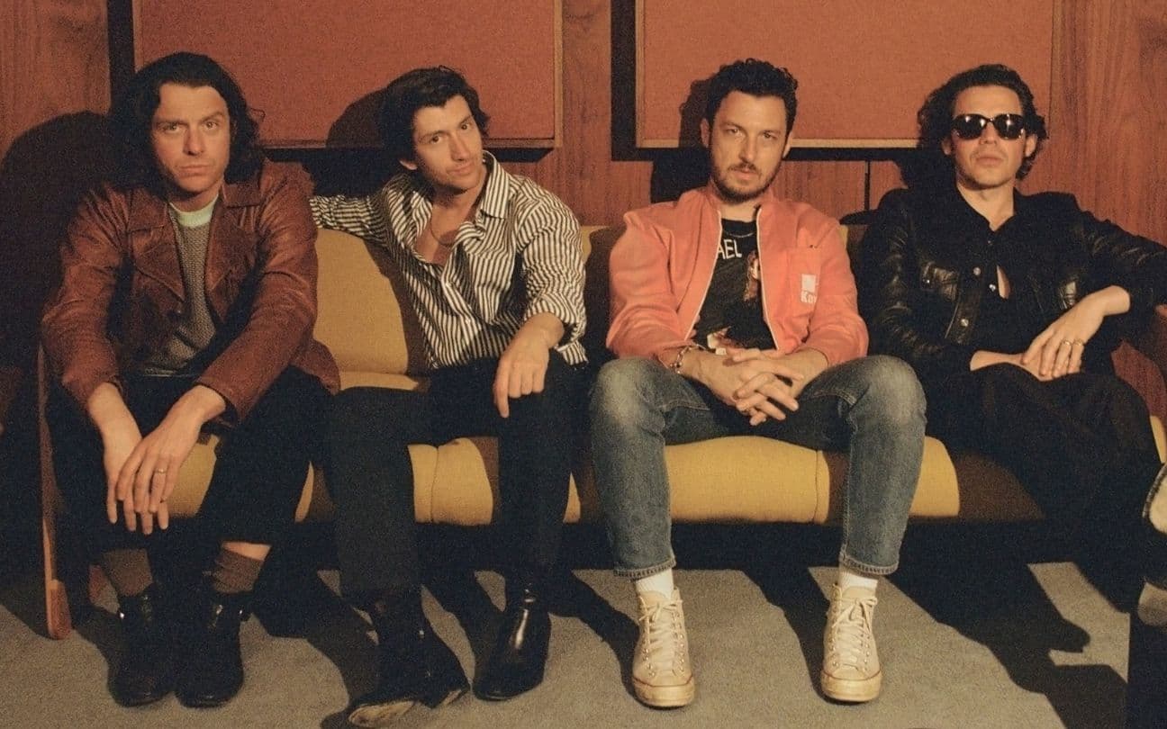 Integrantes do Arctic Monkeys sentados em um sofá