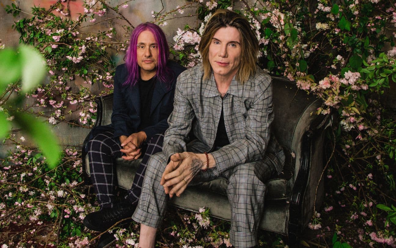 Integrantes do Goo Goo Dolls sentados em um sofá com flores ao redor