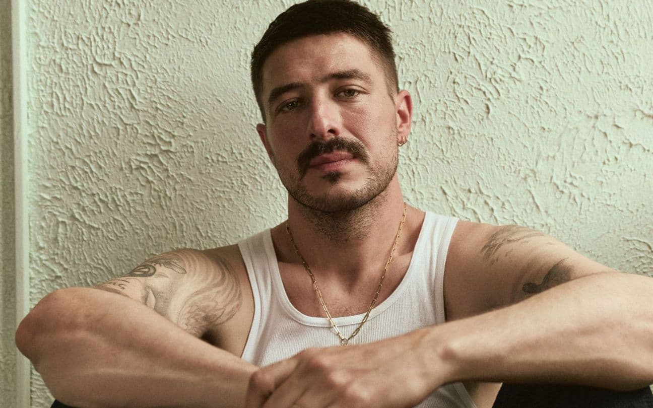 O cantor Marcus Mumford sentado, encostado na parede