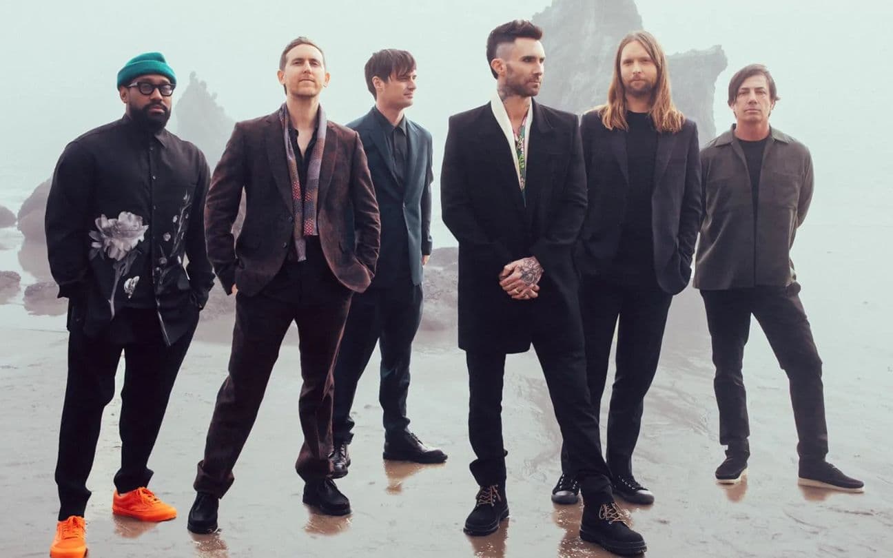 Membros do Maroon 5 em pé em uma praia
