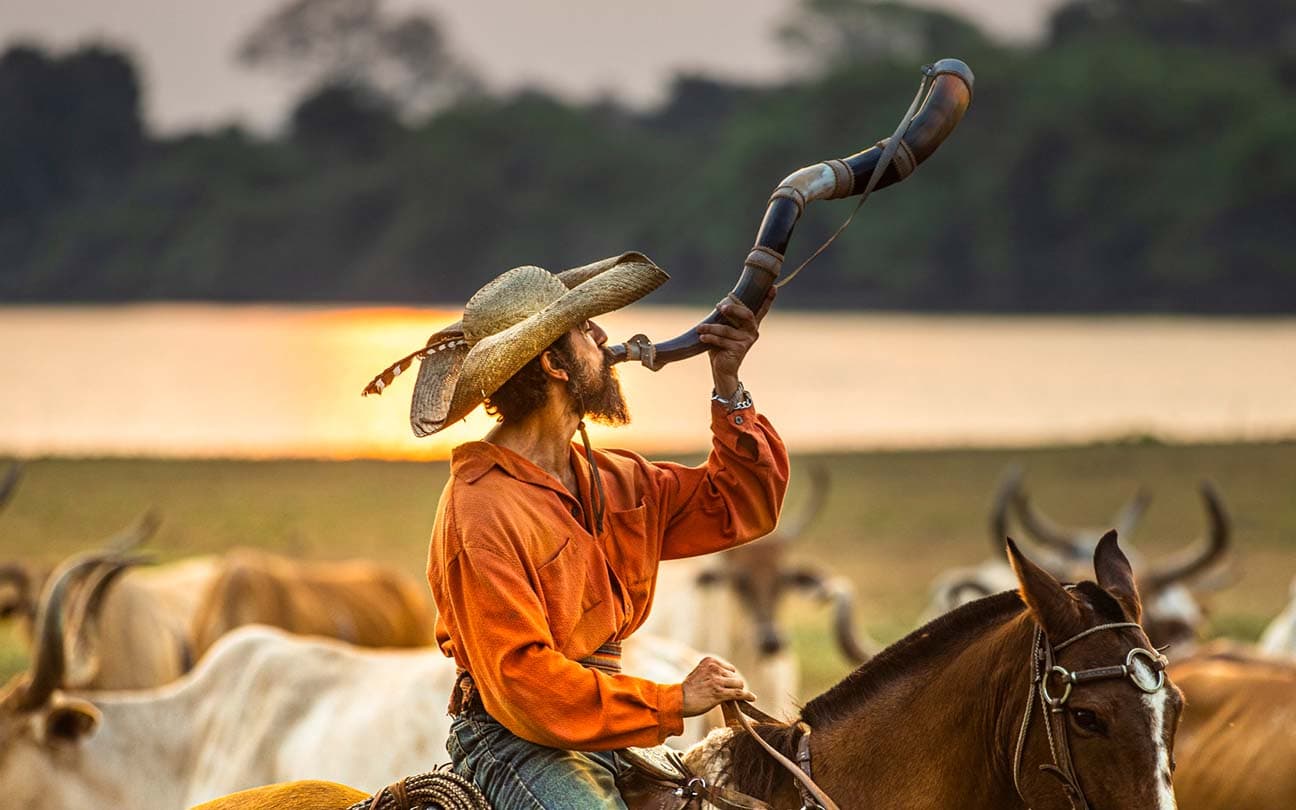 O ator Irandhir Santos, como Joventino, toca berrante em cima de um cavalo em cena no final da tarde em Pantanal