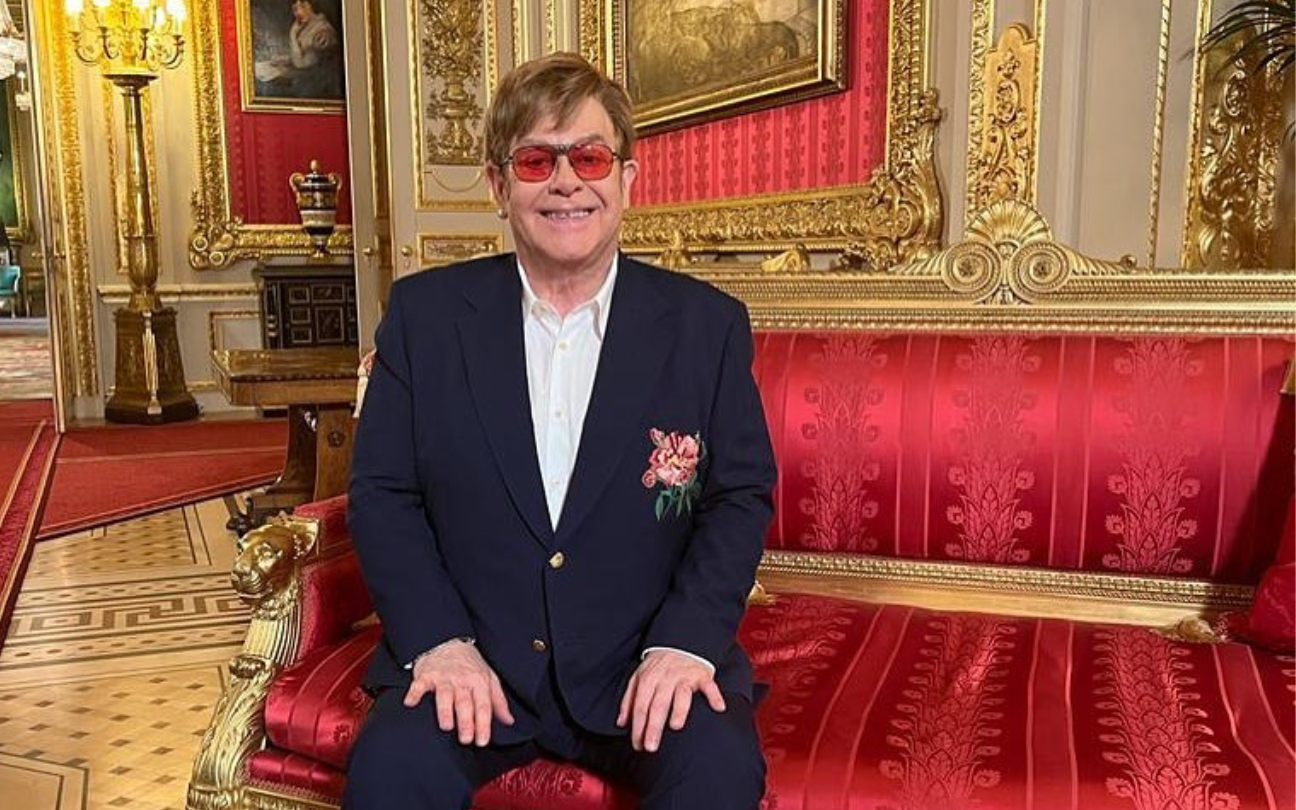 P cantor Elton John sorri para uma foto, sentado em um sofá