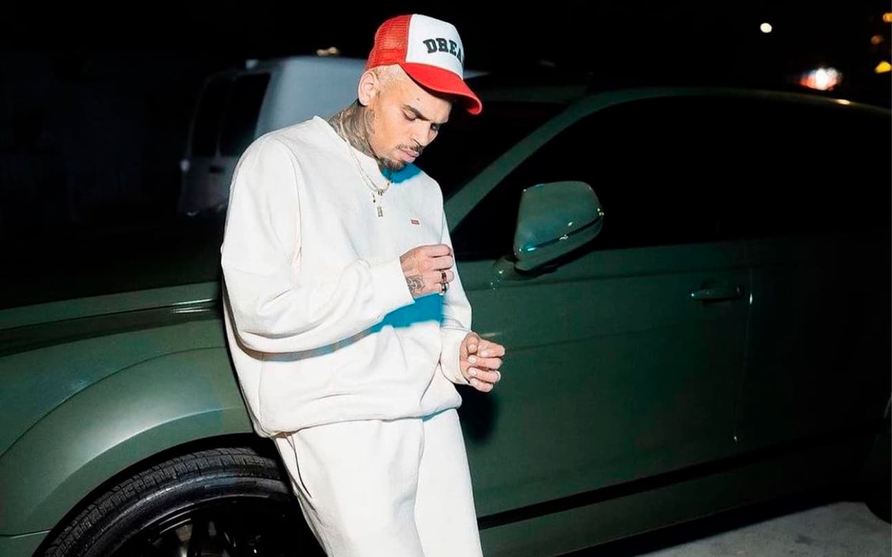 Chris Brown olhando para o chão, encostado em carro